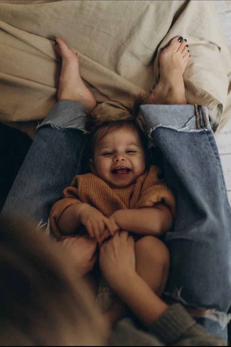A smiling baby cradled between a parent’s legs